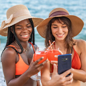 Delighted diverse girlfriends with cocktails taking selfie near sea Travel AI Assistant